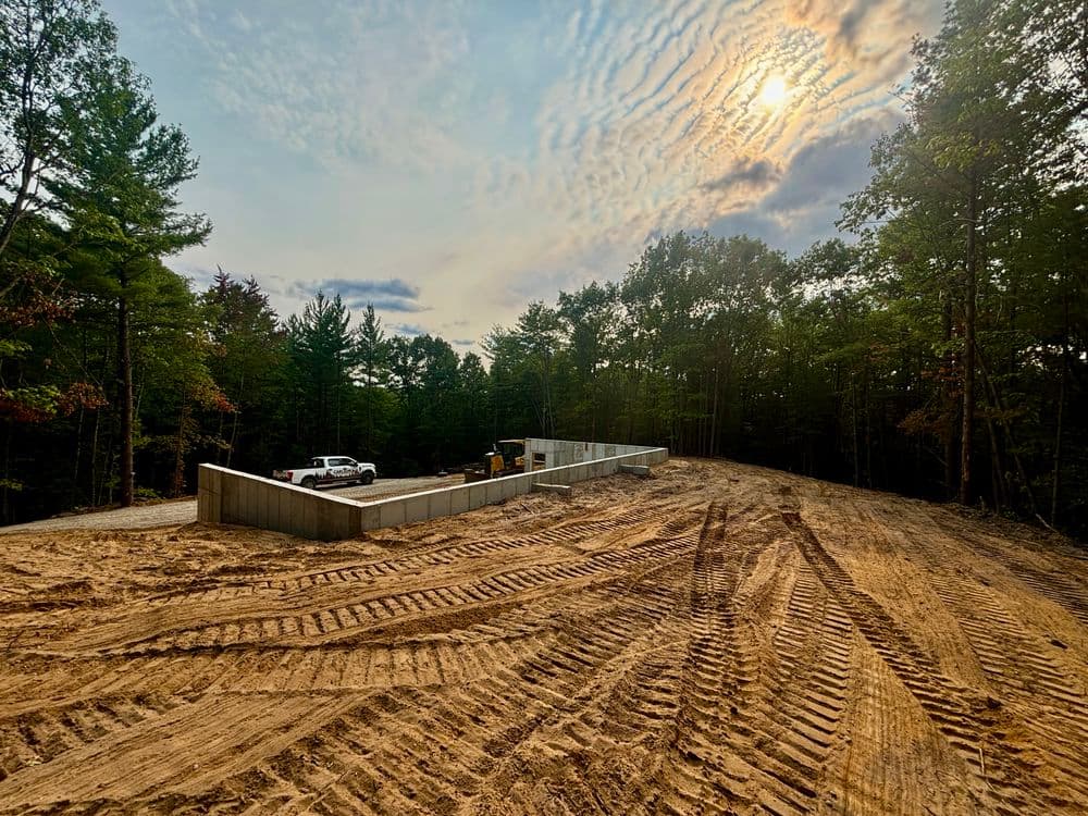 Newly cleared construction site with foundation walls and tire tracks under a sunset sky.